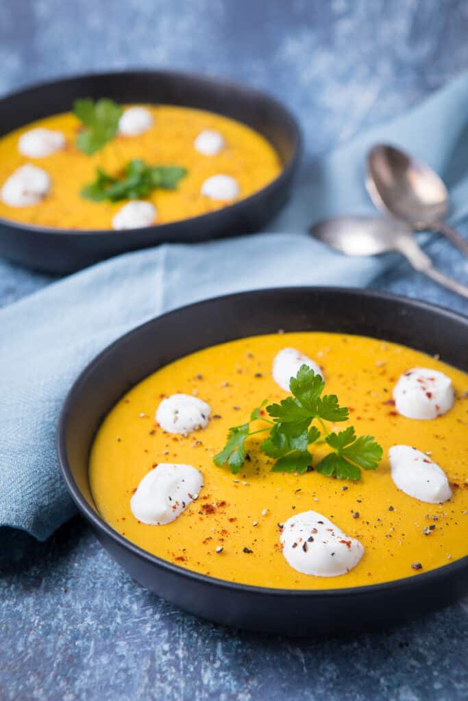 Two bowls of yellow Lebanese Lentil Soup with dollops of cream